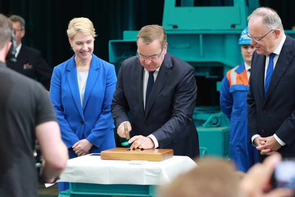 Im Rahmen der traditionellen Kiellegung nagelt Verteidigungsminister Pistorius, neben den weiteren Ehrengästen, eine Münze auf ein Holzbrett - Blauer Bund